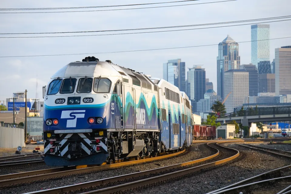 A blue and white Sound Transit heavy rail commuter trail with downtown Seattle skyline in background.